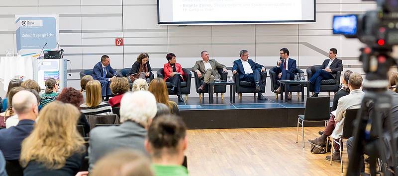 Podiumsdiskussion auf der Bühne mit Publikum davor