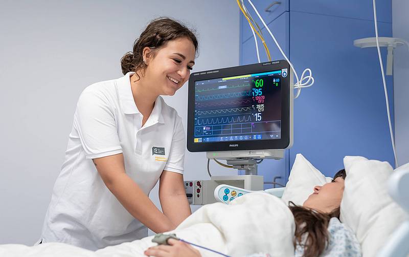 Eine Krankenpflegerin am Bett einer Patientin. Nebenan steht ein Monitor