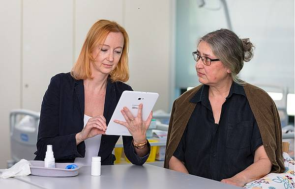 Eine Frau und ihre Betreuerin, die Betreuerin schaut auf ein Tablet