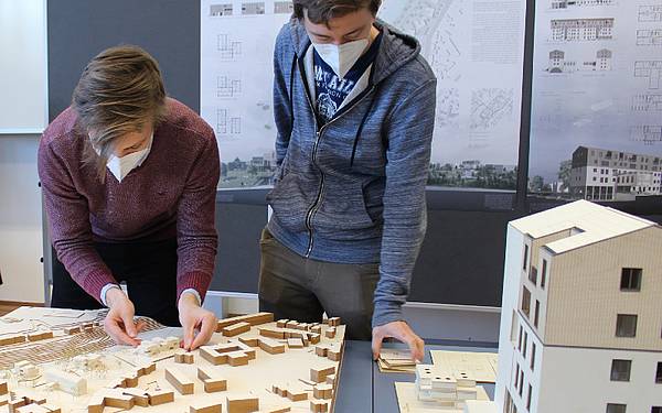 Zwei Studierende vor ihren Architekturmodellen und Plänen