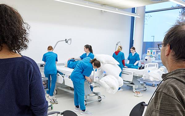 Studierende in eeinem Raum üben an Krankenbetten pflegerische Fertigkeiten