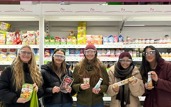 Studierende mit Simulationsbrillen stehen vor einem Kühlregal in einem Supermarkt
