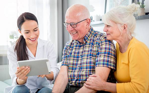 moblie Krankenpflegerin erklärt einem älteren Paar etwas auf einem Tablet