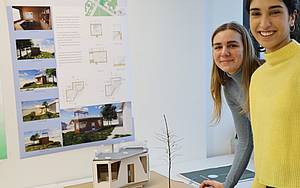 Studierende vor einem selbstentworfenen Modell eines Arbeitsraumes im Grünen, Pläne an der Wand