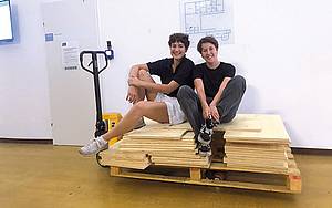 Christa Hörburger und Andreas Dorsch sitzen lachend auf einem Stapel Holzbretter im Start-up Corner