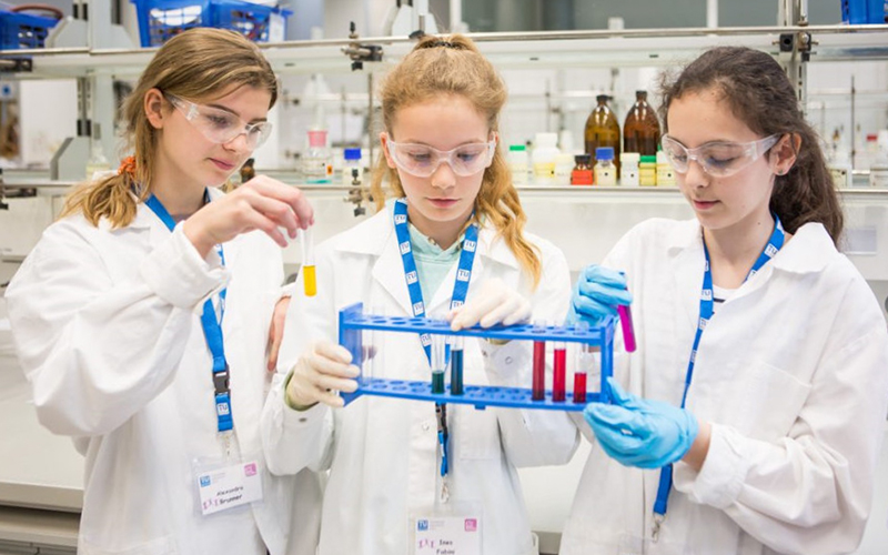 Drei Mädchen in Laborkitteln in einem Chemielabor hantieren mit Reagenzgläsern