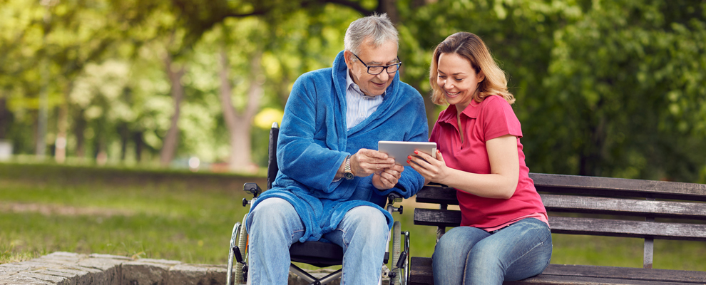 © Lucky Business/www.shutterstock.com Mann im Rollstuhl hält ein Tablet und spricht mit Betreuerin