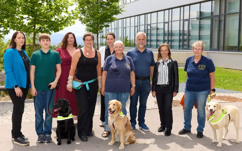 9 Personen und 3 Hunde vor dem Gebäude der FH Campus Wien