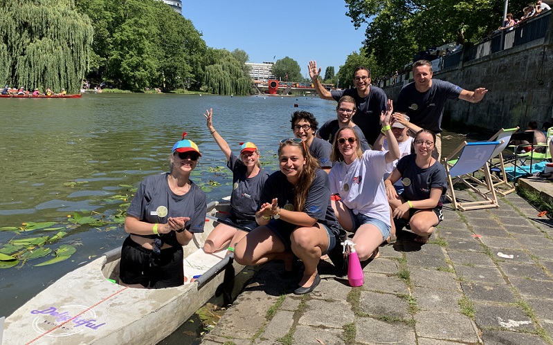 Frauen und Männer in einem Betonkanu und am Ufer an einem Fluss