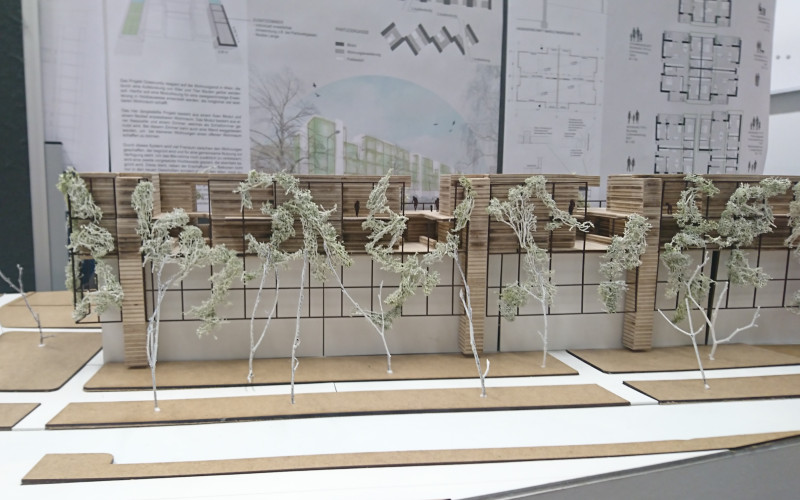 Architektenmodell von einem Wohnhausblock mit Bäumen im Vordergrundund dahinter Pläne an einer Pinwand
