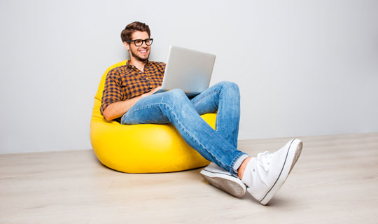 junger Mann mit Brille sitzt mit Laptop auf gelbem Sitzsack