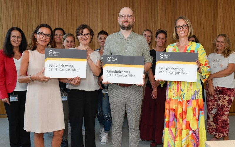 eine Menschengruppe mit Tafeln "Lehreinrichtugn der FH Campus Wien"